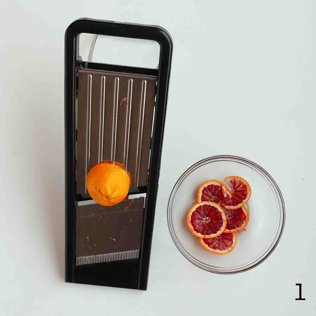 Slices of blood orange in a bowl and half and orange on a mandoline.