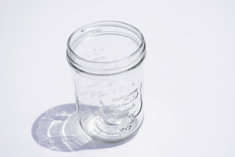 High-angle shot of an empty clear glass jar casting a shadow on a white surface.