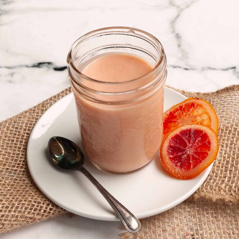 A jar filled with blood orange curd with two orange slices on the side.