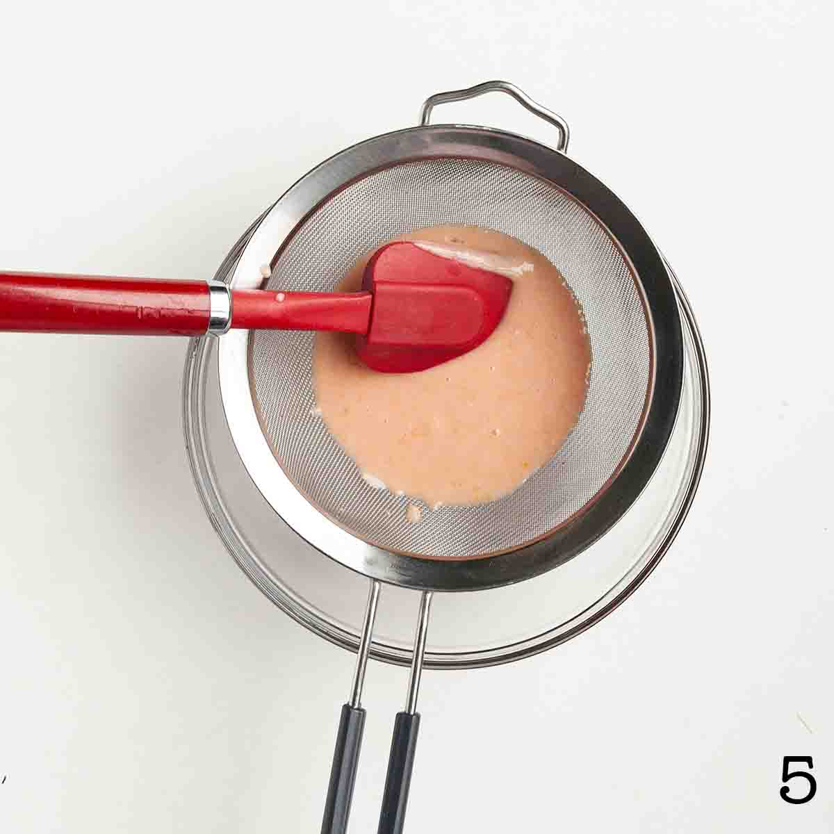 Blood orange curd being strained through a fine mesh sieve.