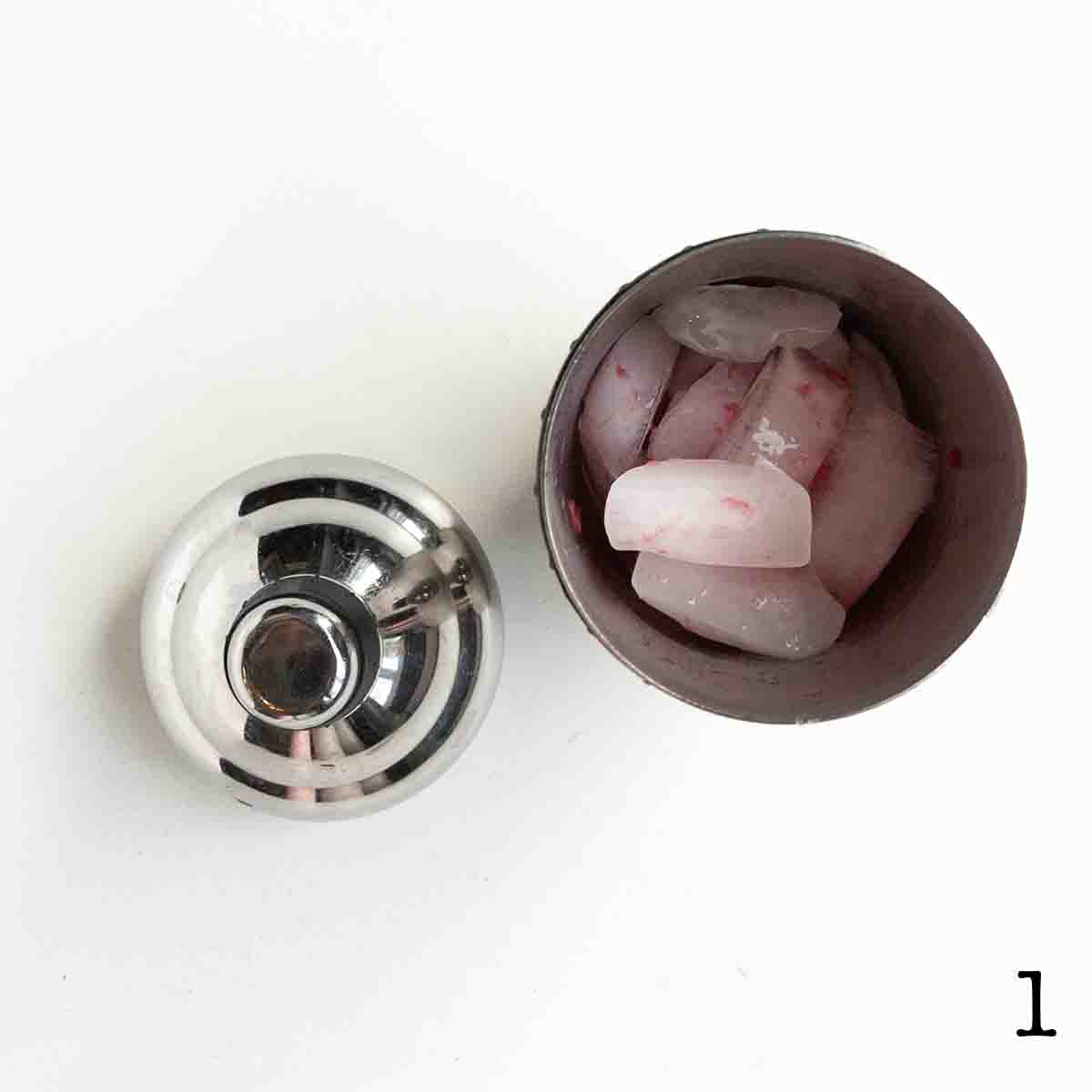 A cocktail shaker with ice and pink liquid.