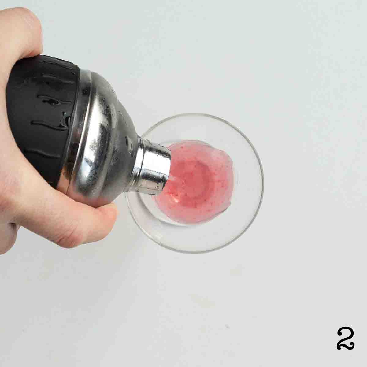 A person pouring a drink from a cocktail shaker into a glass.