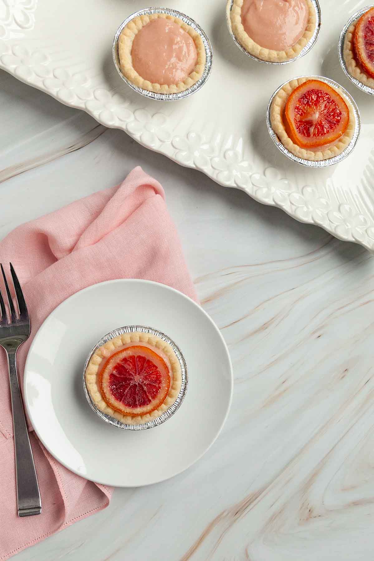 An orange tartlet on a plate with more on a platter nearby.