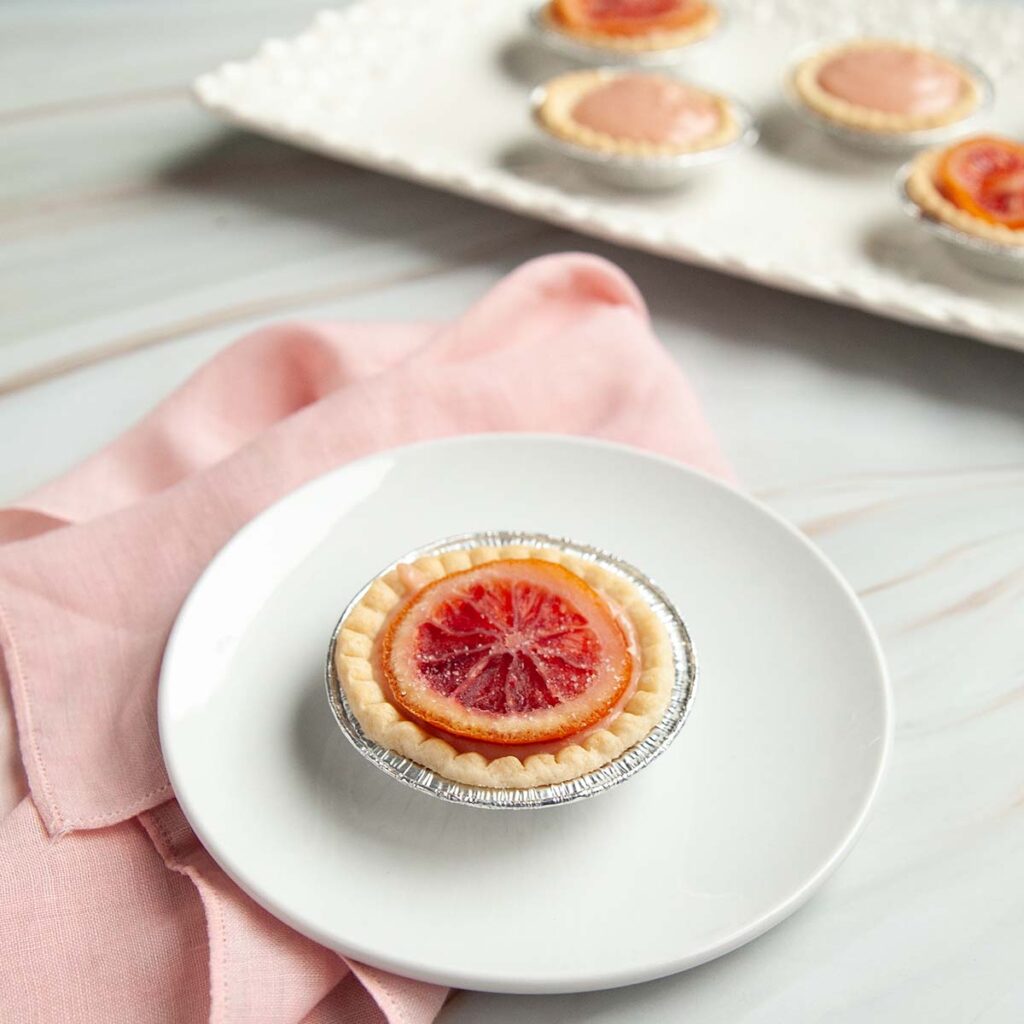 An orange tartlet on a plate with more on a platter nearby.