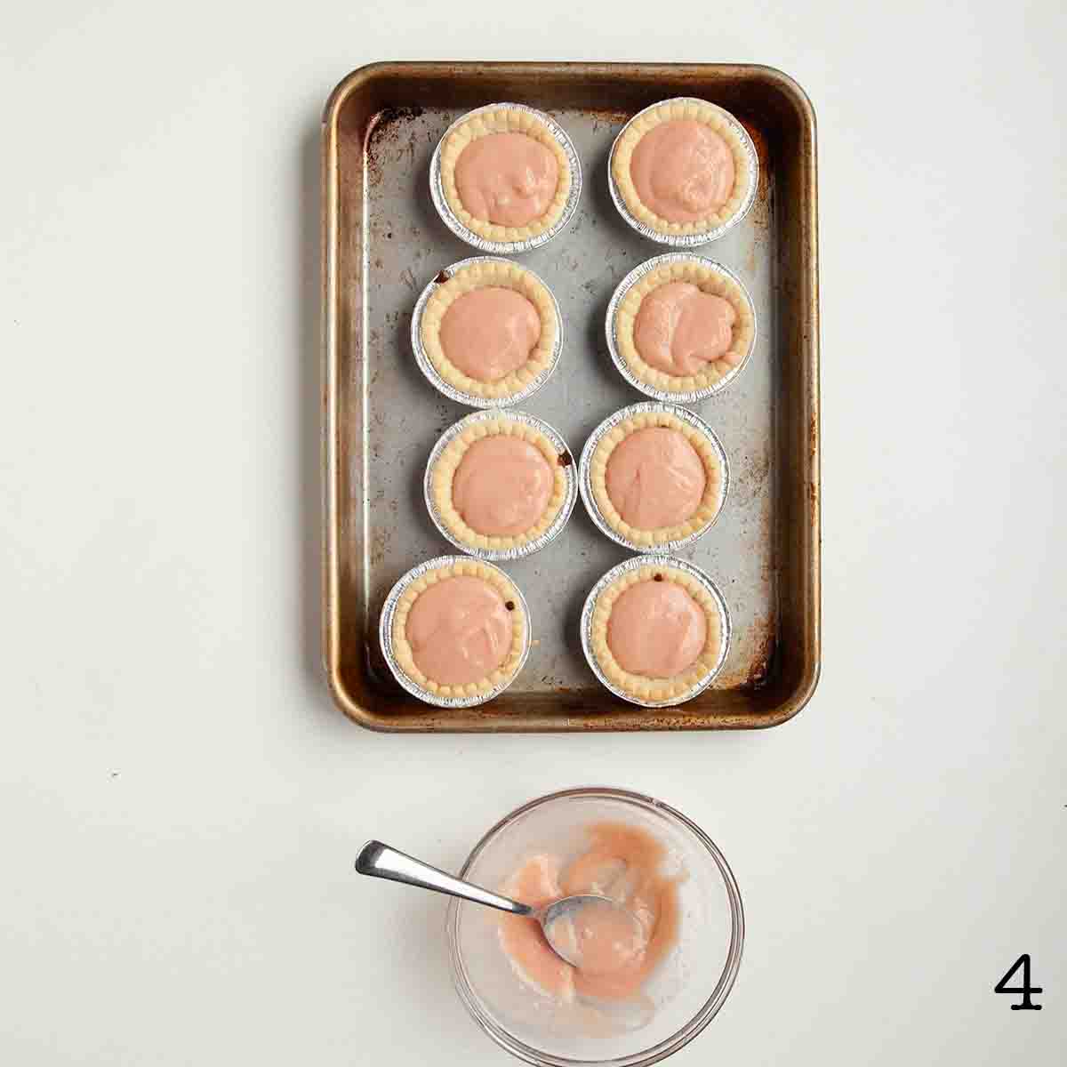 Eight tart shells filled with blood orange curd on a baking sheet.