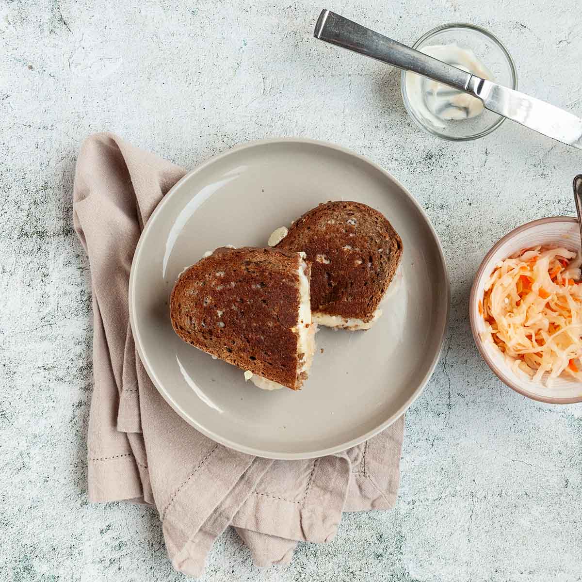 A halved grilled cheese sandwich with sauerkraut on a plate.