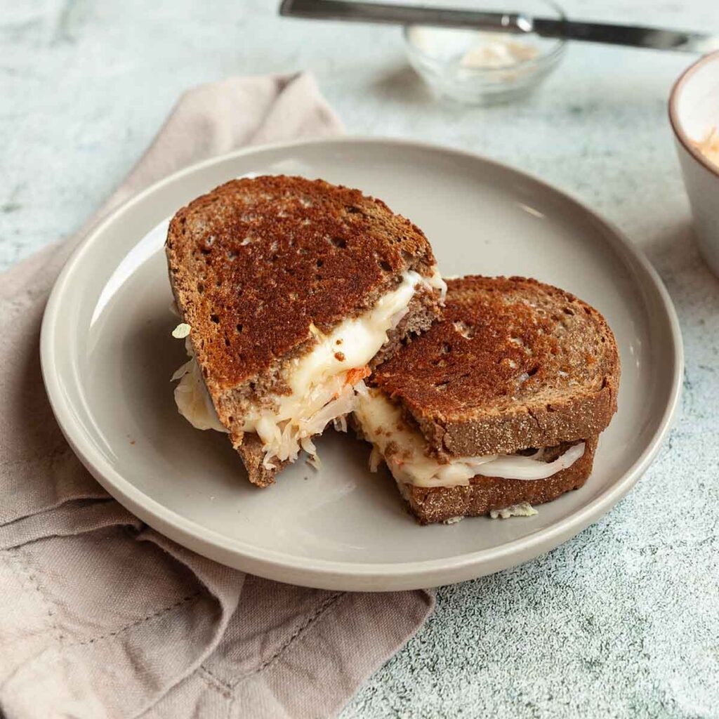 A halved grilled cheese sandwich with sauerkraut on a plate.