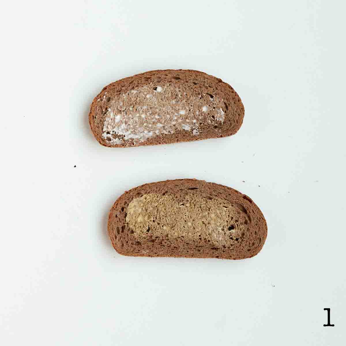 Two slices of rye bread; one spread with mayo and one with mustard.