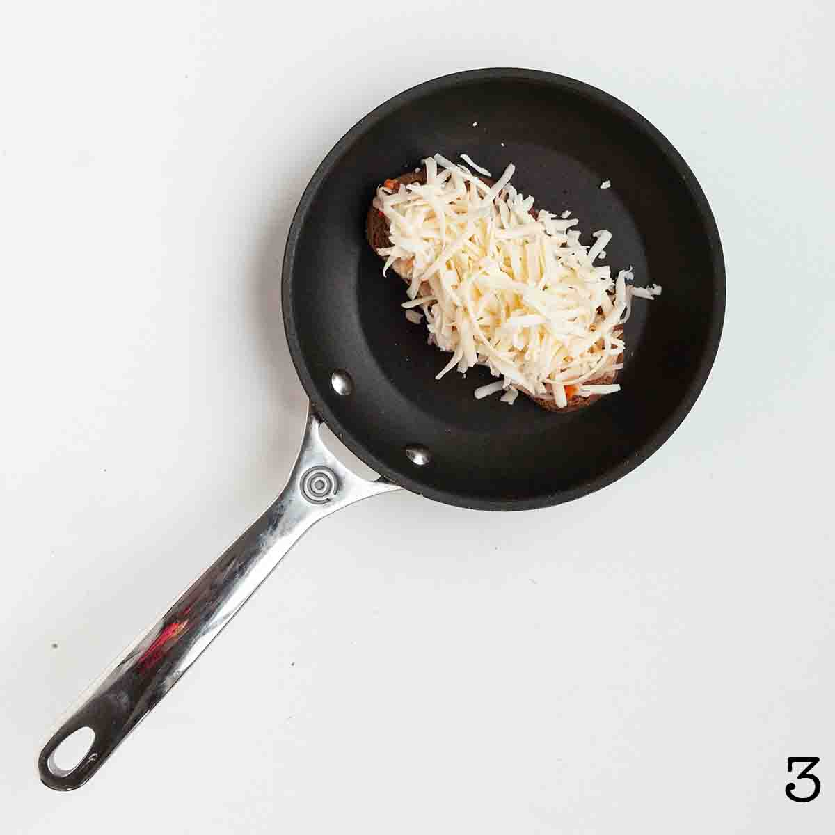 Rye bread topped with grated Swiss cheese in a skillet.