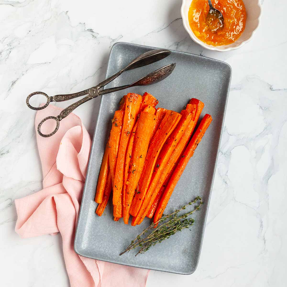 A platter of roasted carrots with a dish of marmalade on the side.