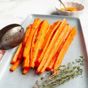 A platter of roasted carrots with a dish of marmalade on the side.