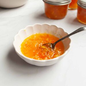 A dish of orange and lemon marmalade with a spoon resting inside.