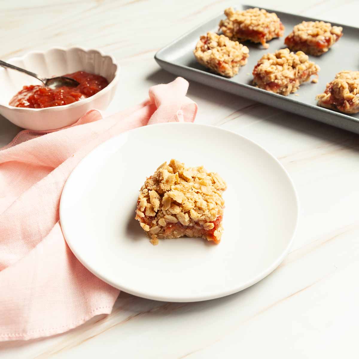 A rhubarb oat bar on a small plate with a platter of oat bars nearby.