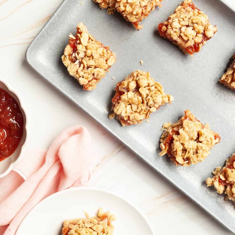A rhubarb oat bar on a small plate with a platter of oat bars nearby.