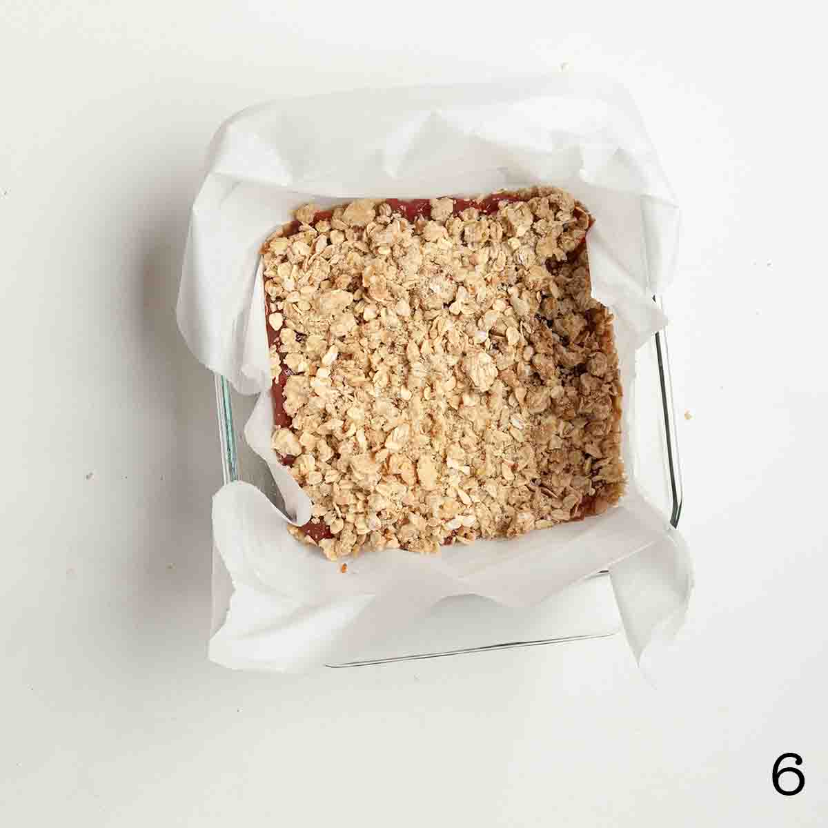 Oat crumble on top of jam in a square baking dish.