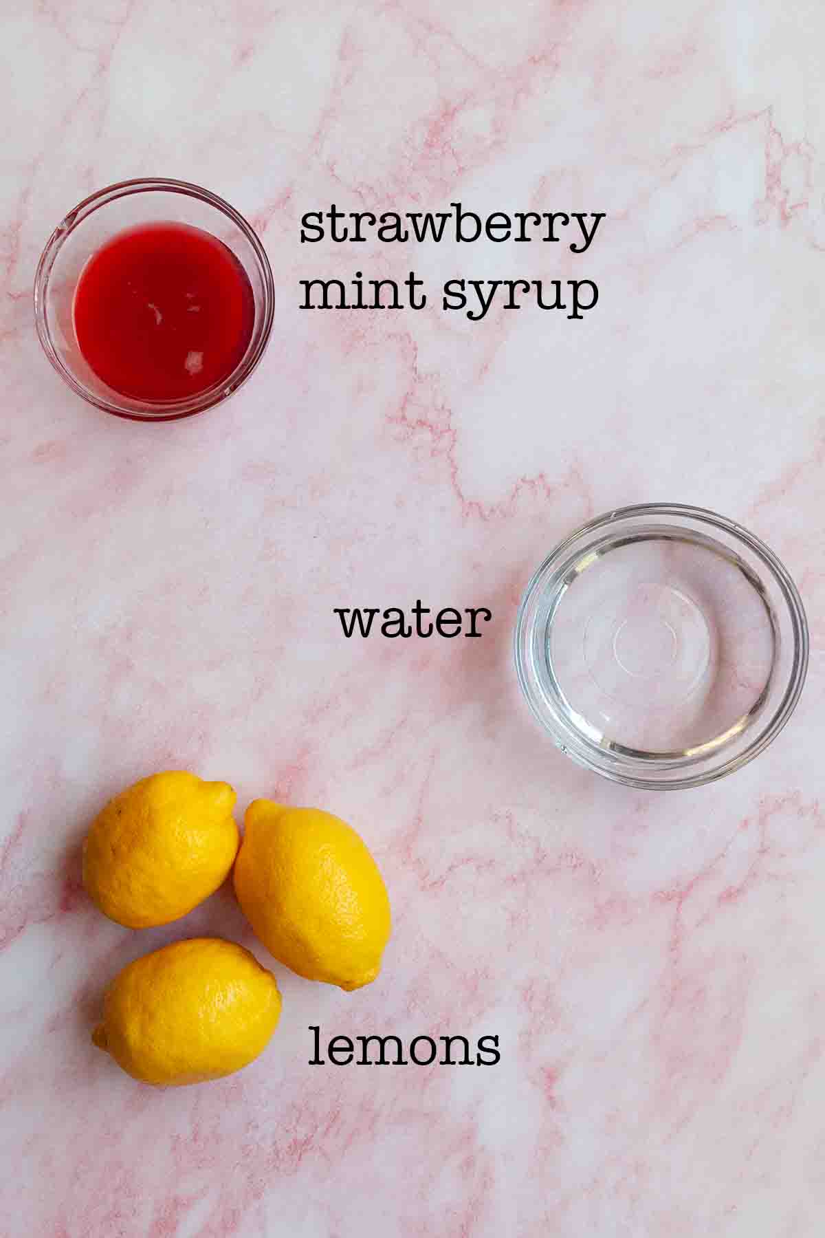 Ingredients for strawberry mint lemonade--strawberry mint syrup, water, and lemons.