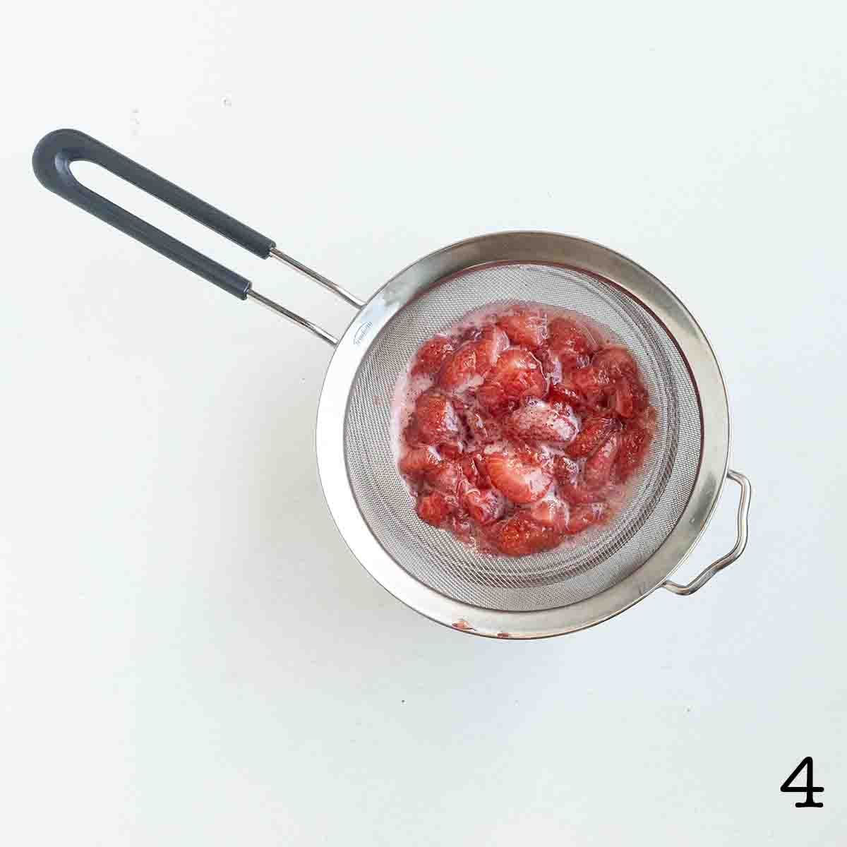 Strawberry syrup draining through a fine mesh sieve.