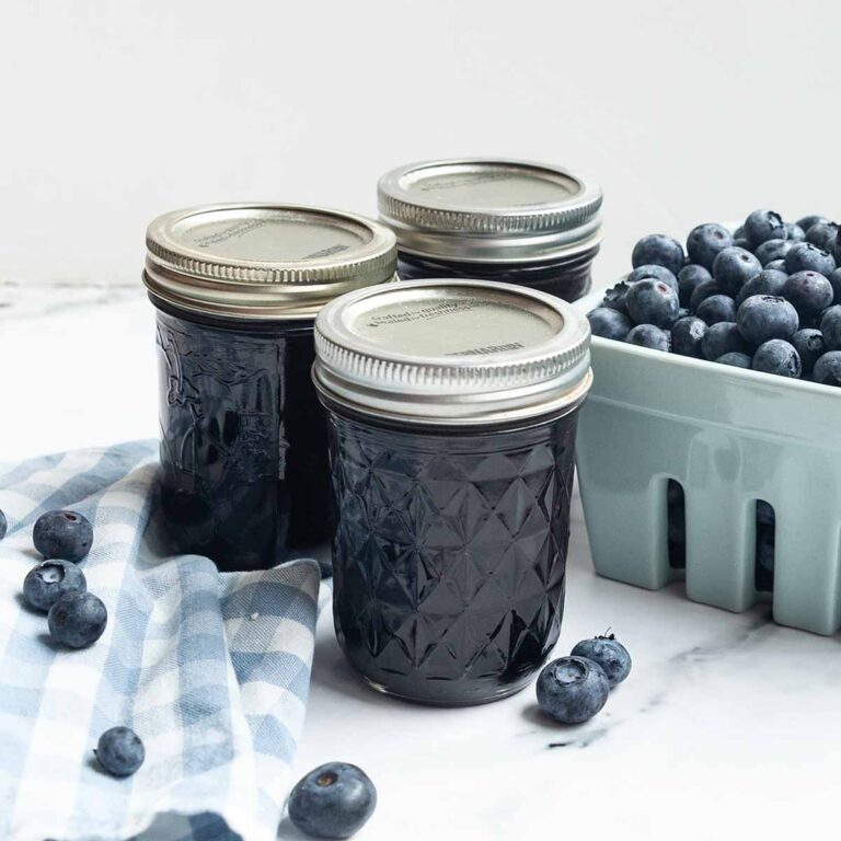 Three jars of jam and a basket of blueberries.