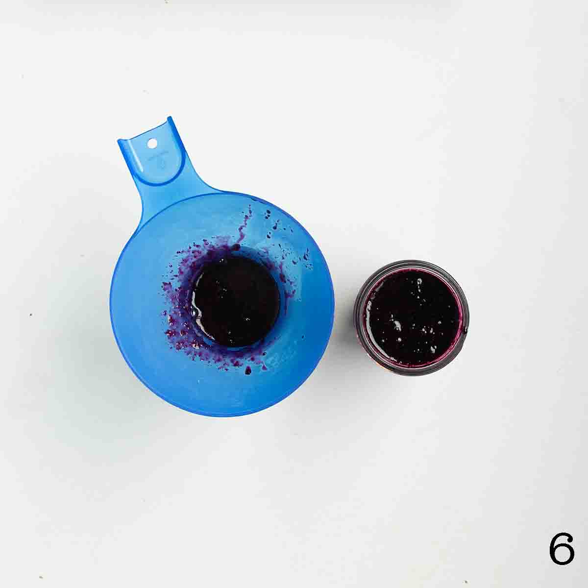 Jars of jam being filled with blueberry jam.