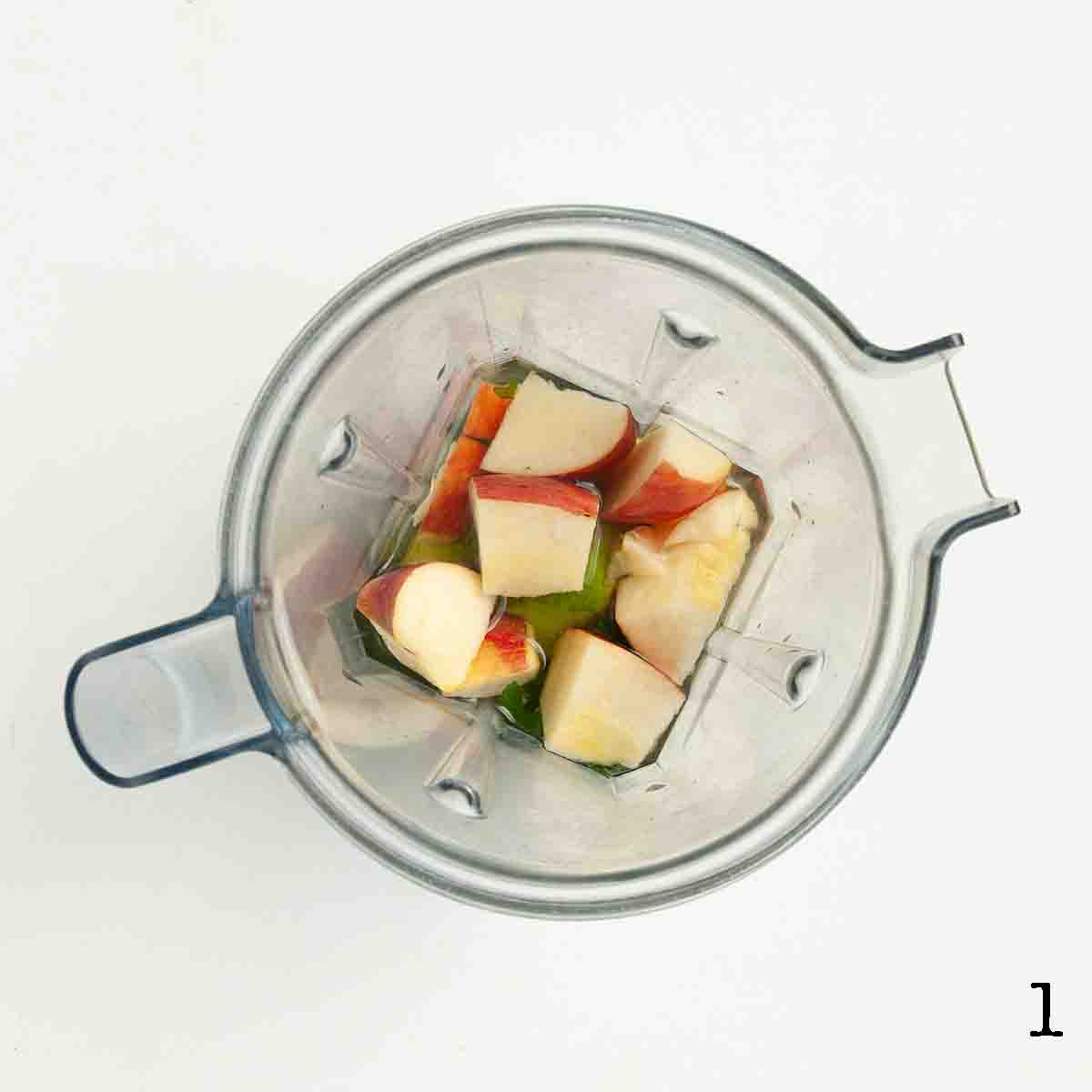 Chunks of apple in a blender with avocado and apple juice.