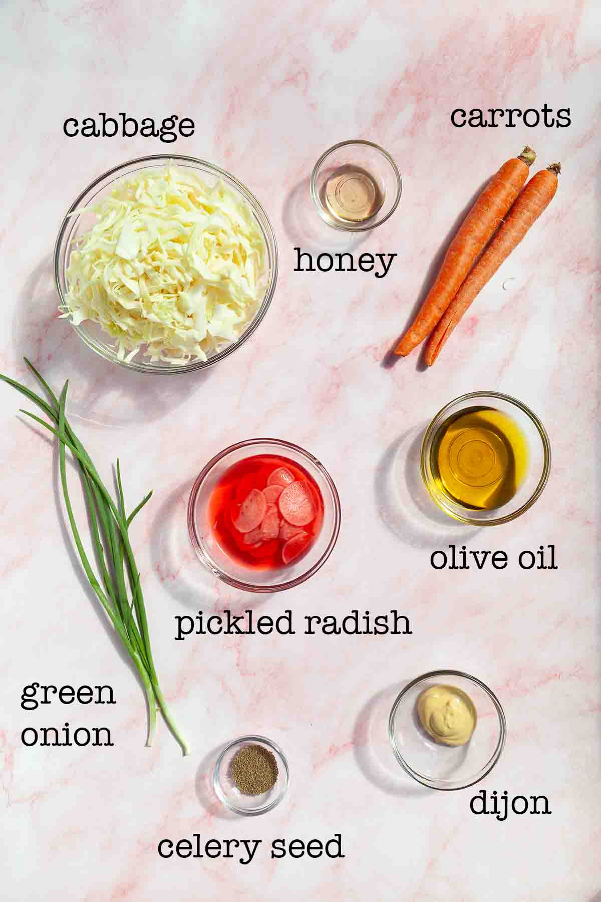 Ingredients for pickled radish slaw--cabbage, honey, carrots, green onion, pickled radish, olive oil, celery seed, and dijon mustard.