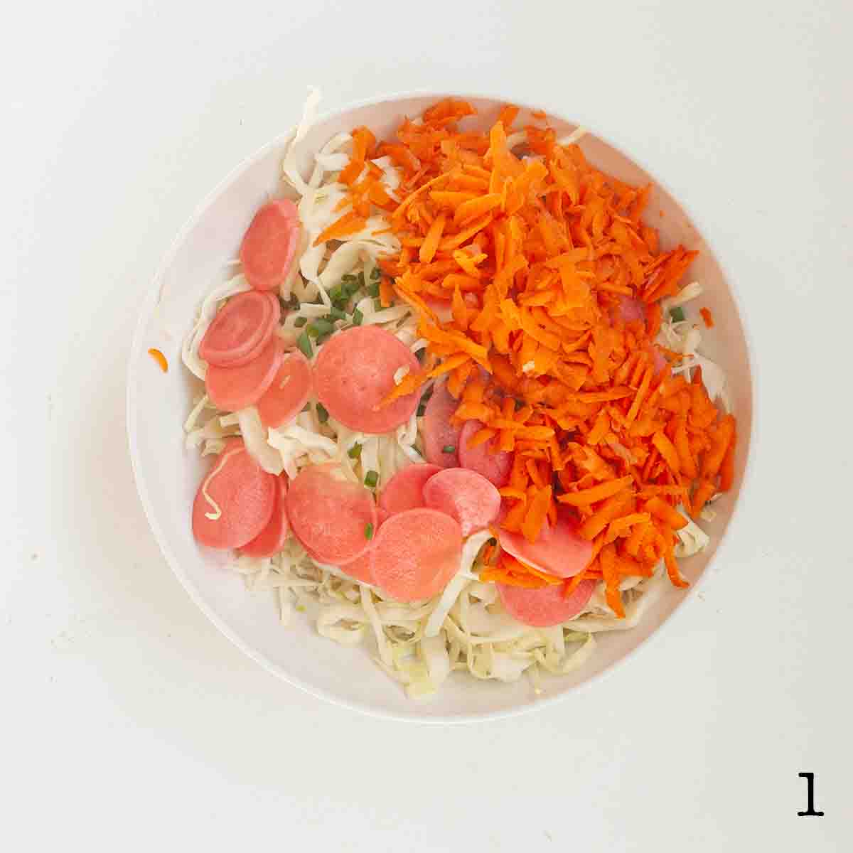 A bowl of cabbage, shredded carrot, and sliced pickled onion.