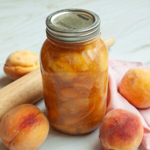 A jar of peach pie filling with peaches around it.