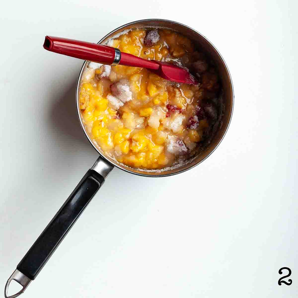 Peaches, raspberries, and sugar in a pot.