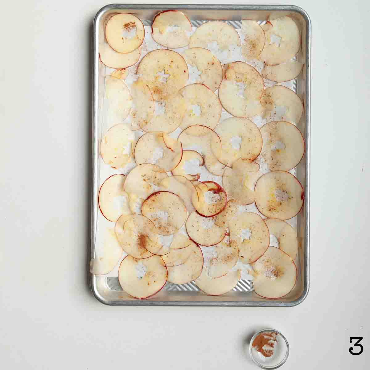 Thin slices of apple dusted with cinnamon on a baking sheet.