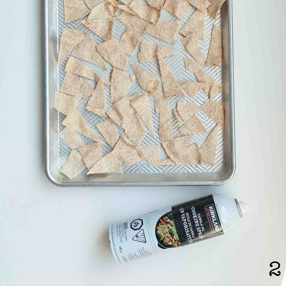 Pieces of pita bread cut into triangles on a baking sheet, with a can of cooking spray nearby.