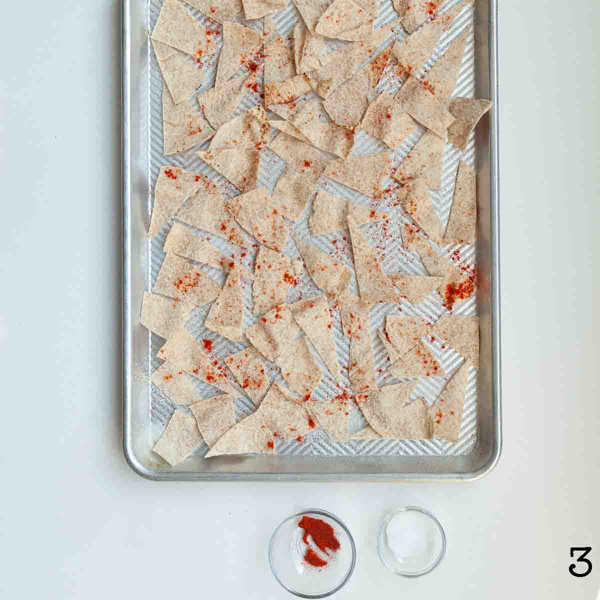 Pieces of pita bread cut into triangles on a baking sheet with salt and paprika sprinkled on top.