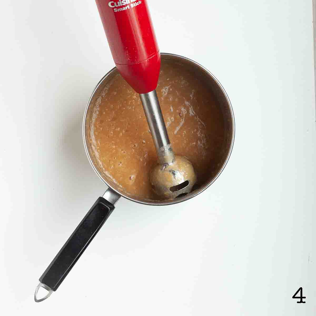 Blended applesauce in a pot with an immersion blender resting inside.
