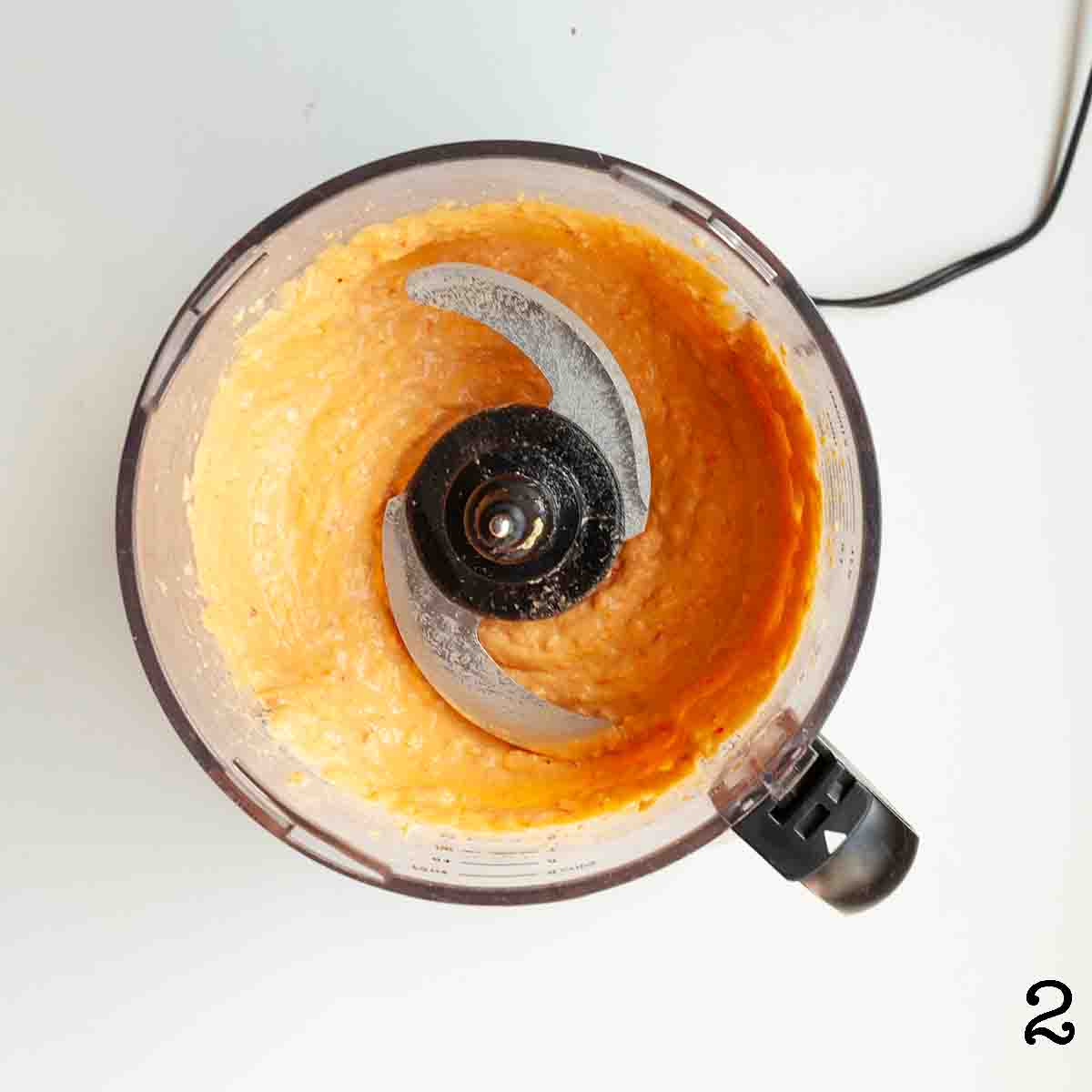 A food processor with smooth roasted red pepper hummus.