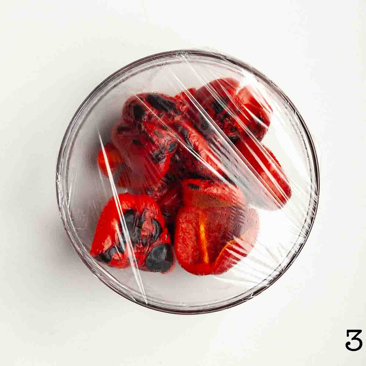 Roasted red peppers in a large bowl, covered with plastic wrap.