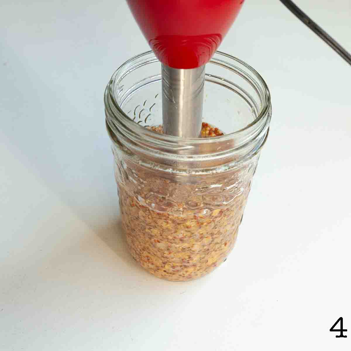 A jar of homemade mustard with an immersion blender submerged in it.