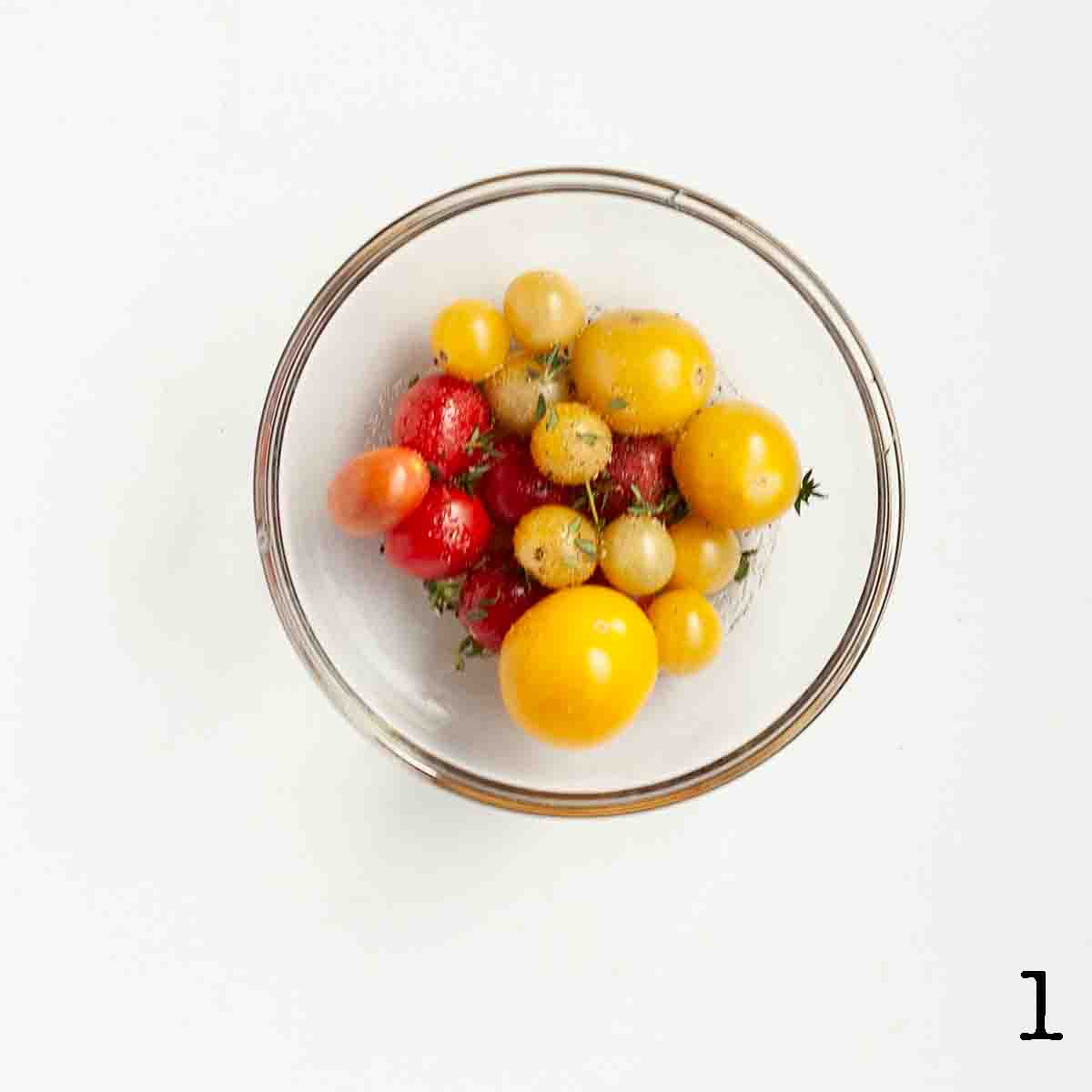 A bowl of cherry tomatoes with oil and thyme leaves.