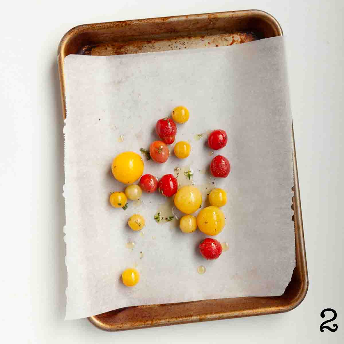 Cherry tomatoes coated with oil on a parchment-lined baking sheet.